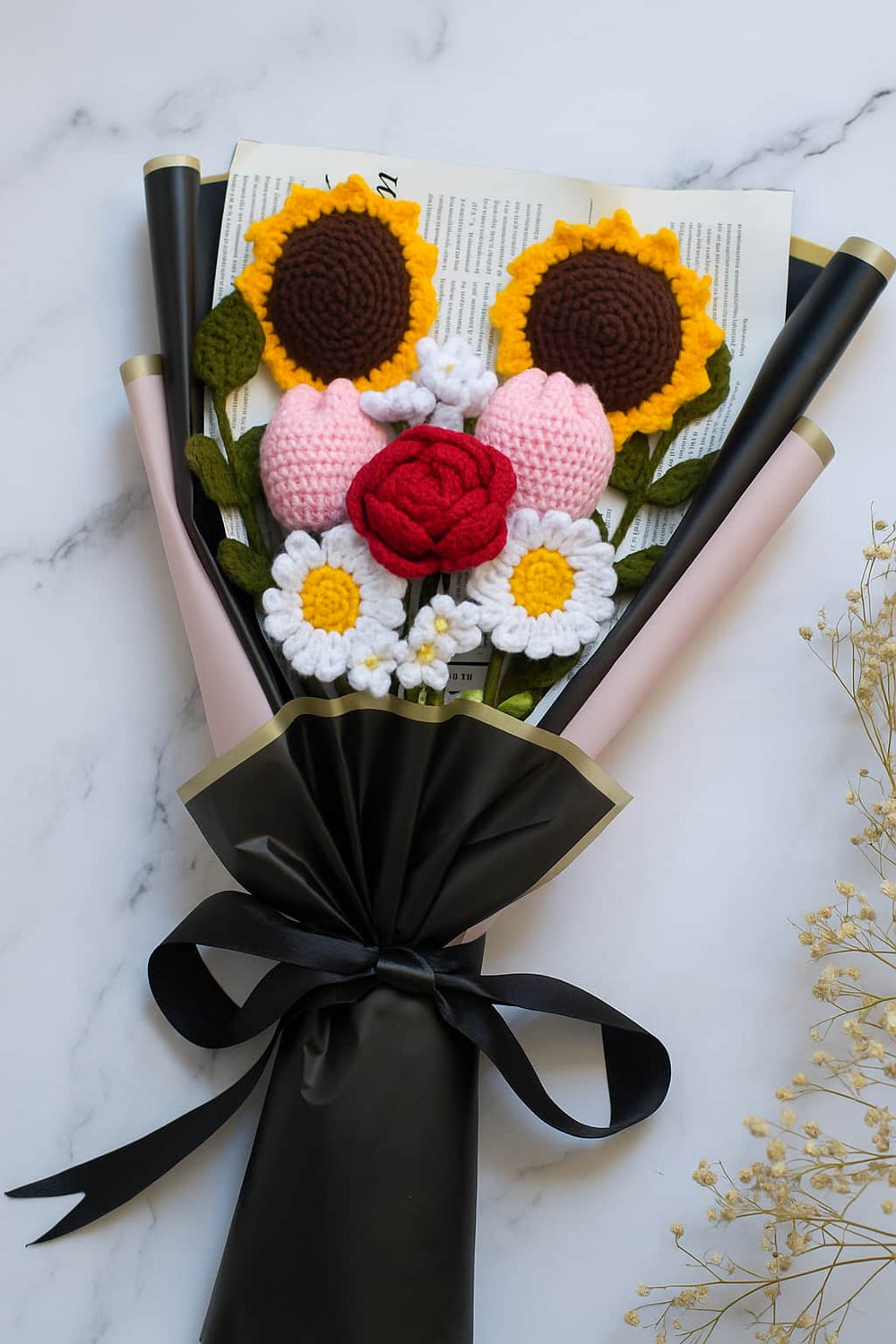 Bouquet of crocheted flowers on a book with a black ribbon on a marble background