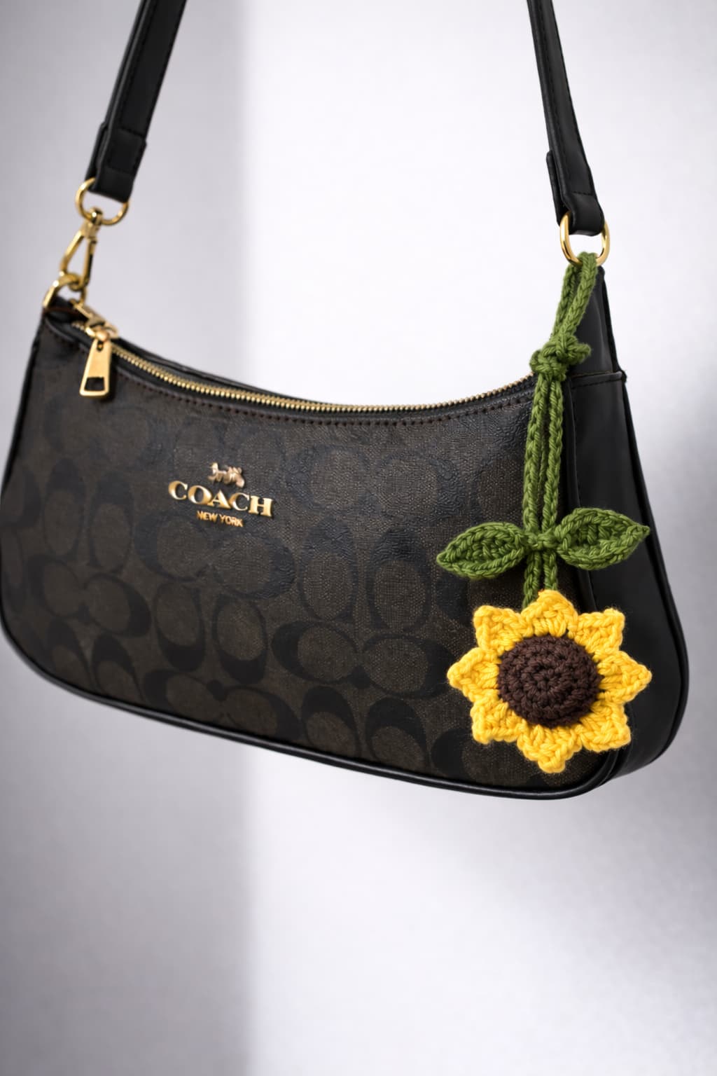Close-up of the textured brown center and yellow petals on the crochet sunflower key charm on coach bag