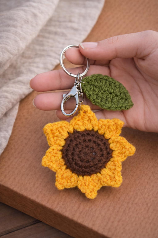 Hand holding a large crochet sunflower keychain with a green leaf charm and silver clasp