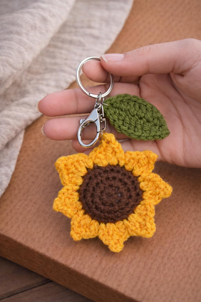 Hand holding a large crochet sunflower keychain with a green leaf charm and silver clasp