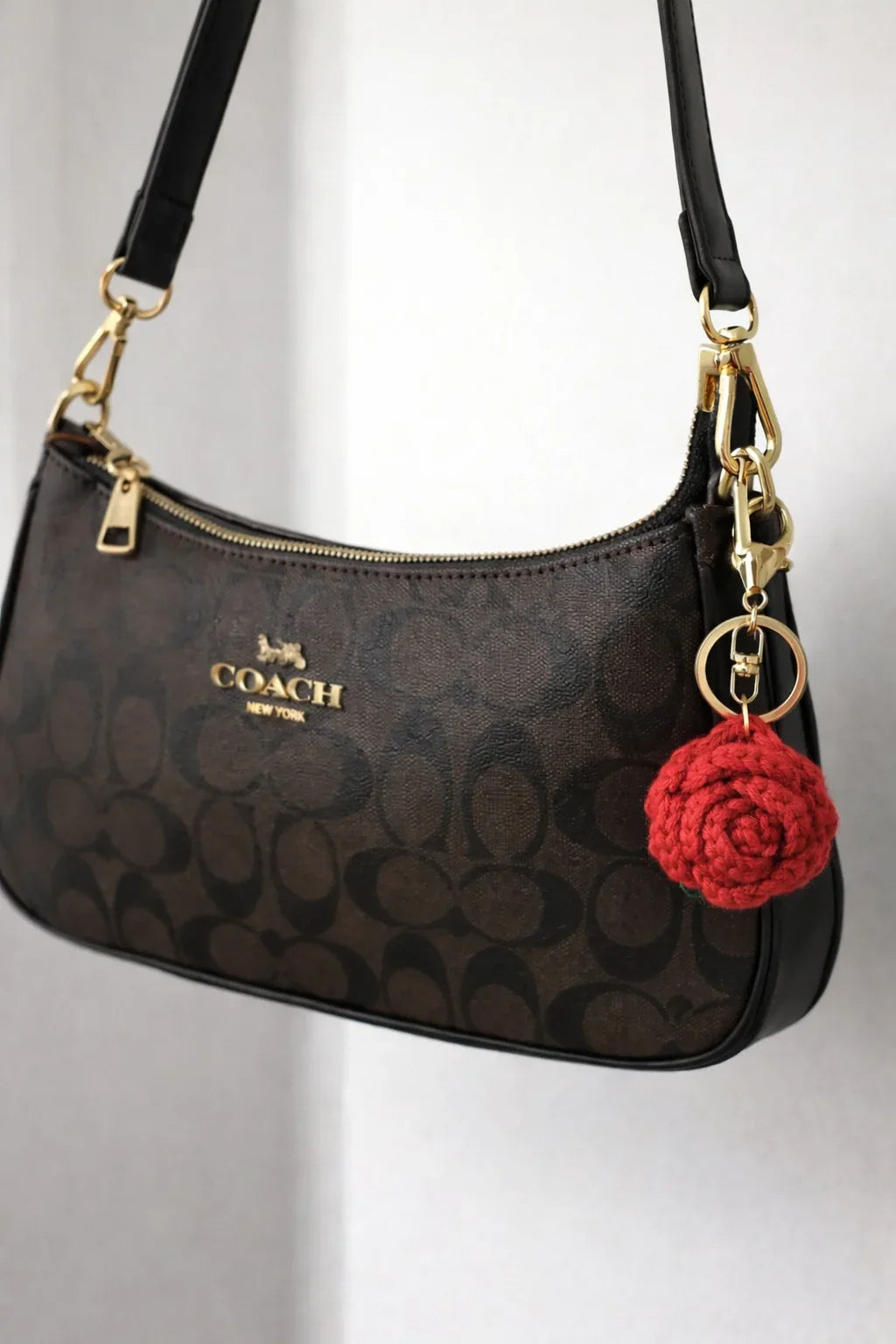 Detailed view of a red crochet rose keychain with green leaves and a silver lobster clasp on a coach bag