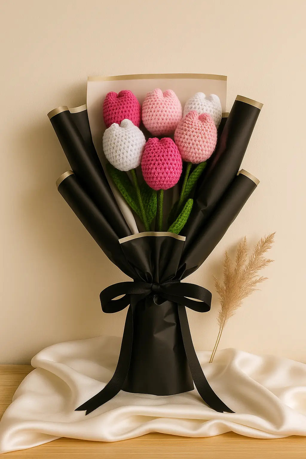 Bouquet of pink, white, and dark pink crochet tulips wrapped in black paper with a bow on a beige background.